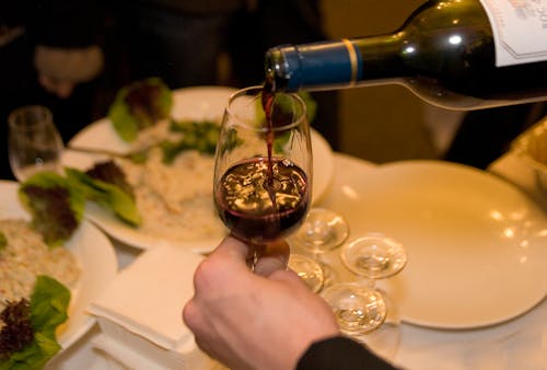 Close-Up Shot of a Person Pouring Red Wine on a Glass