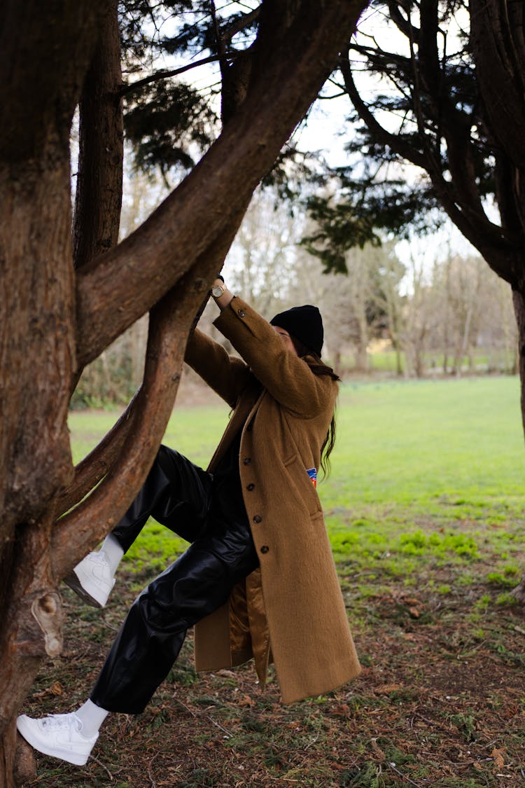 A Woman In Brown Coat Climbing On A Tree