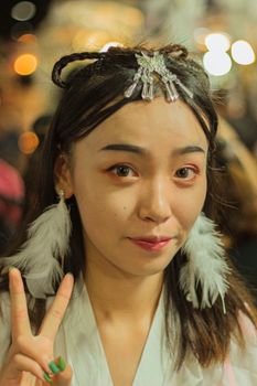 Portrait of a woman with feather earrings making a peace sign at night with a blurred background.