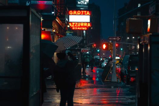 Busy urban city street crowded with pedestrians and illuminated by electric lights in rainy autumn evening