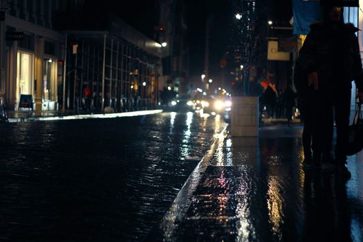 Busy modern city street with pedestrian in warm wear and driving cars in autumn rainy evening