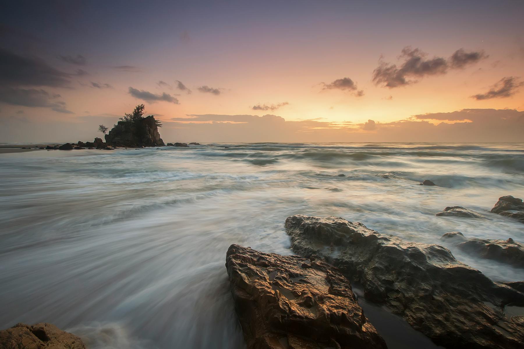 迷人的海洋日出中，光滑的波浪拍打着崎岖的岩石，营造出一片宁静而充满活力的海景