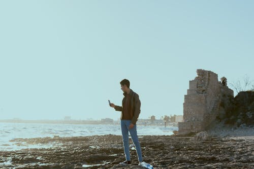 Free A Man in Brown Jacket and Blue Denim Jeans Standing on Sea Stock Photo