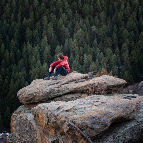 Free A Man in Red Jacket Sitting on Brown Rock Stock Photo