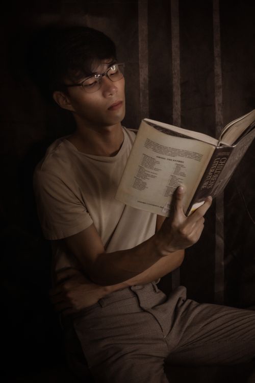 Free Concentrated Asian guy in casual outfit sitting and reading interesting book in dark room at home Stock Photo
