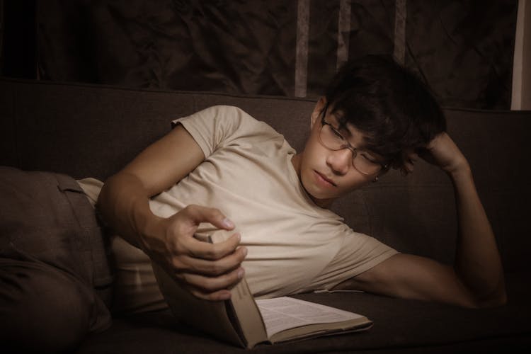 Thoughtful Ethnic Man Reading Book On Couch