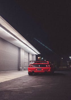 Red Ferrari sports car parked next to a garage under dim street lights at night, showcasing luxury and style.