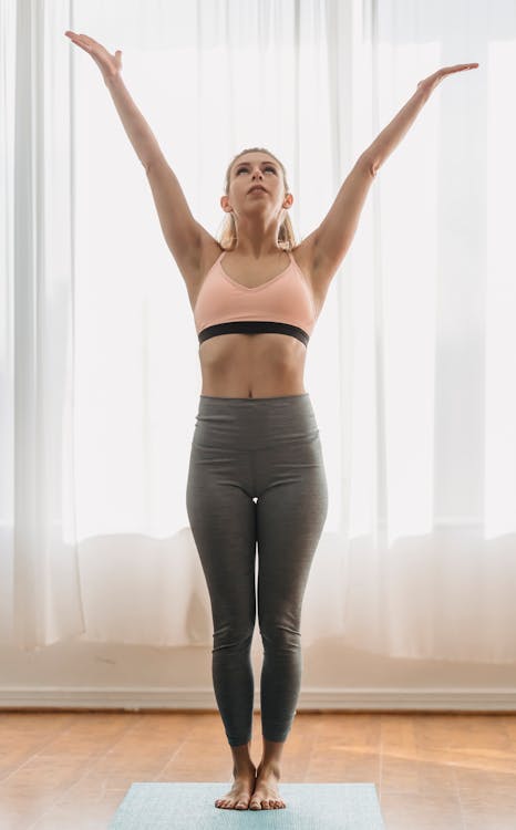 Free Full body of mountain pose with raised arms looking up while standing on mat during yoga training in light room Stock Photo