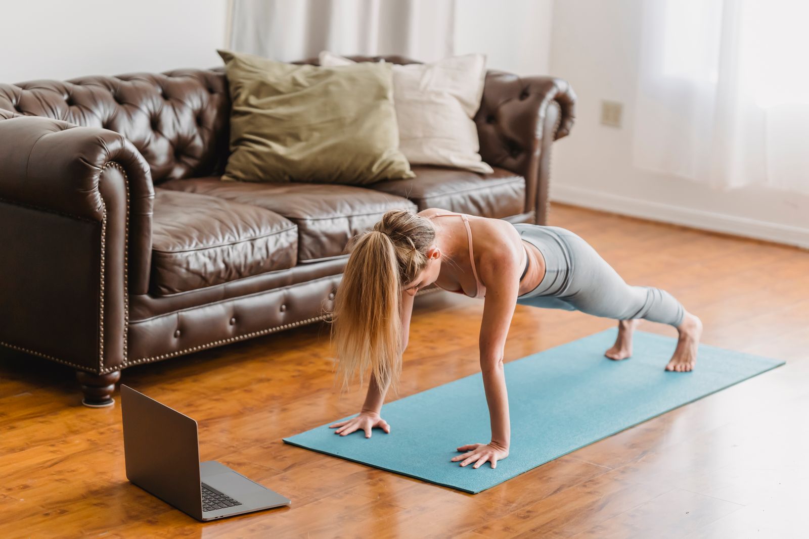 Woman practicing yoga on a mat at home while following an online yoga class on her laptop