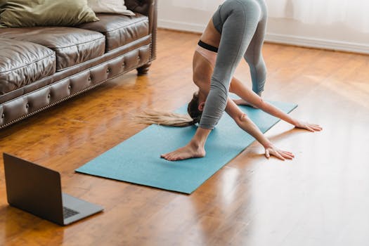 Full body side view wide legged forward bend asana while training on mat in living room with laptop near couch