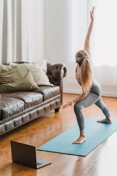 Full body side view of unrecognizable female in activewear practicing extended side angle posture while performing yoga exercise in living room with laptop