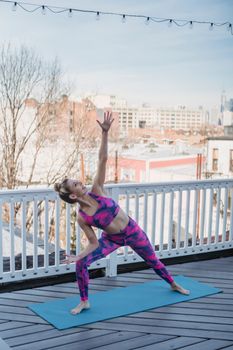 Positive slim female in activewear performing Parsvakonasana for increasing flexibility during yoga session on sports mat on balcony