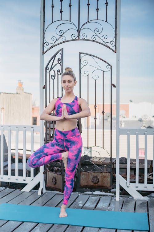 Full body of slim female in activewear practicing Ardha Padmasana during yoga training on terrace