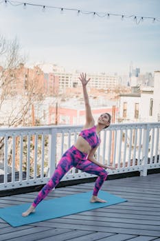 Full body of smiling female practicing Side Angle asana with hands raised up during yoga session on balcony