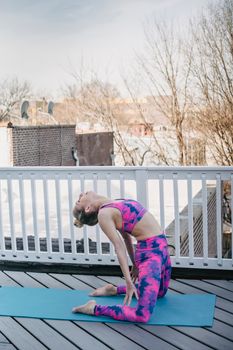 Full body side view of sportive female in activewear practicing Ustrasana on mat during yoga training on wooden terrace