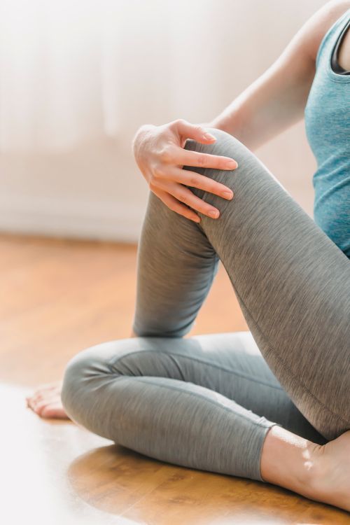 Free Unrecognizable barefoot slim female in sportswear sitting on floor while warming up before yoga training at home in light room Stock Photo