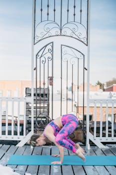 Full body side view of flexible female in sportswear doing Crow asana on mat during yoga training against residential buildings