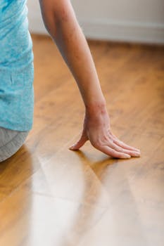 Crop anonymous female resting on wooden floor and leaning on fingers during training in sport studio