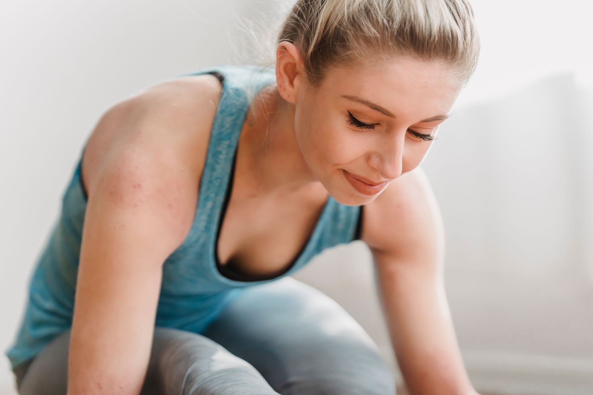 Crop smiling female athlete leaning forward and looking down while squatting in light fitness studio