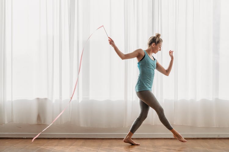 Cheerful Woman With Gymnastic Ribbon Stepping On Wooden Floor