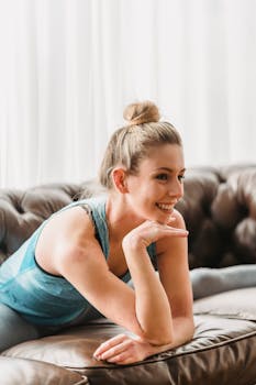 A cheerful young woman in activewear smiling while lounging on a sofa.