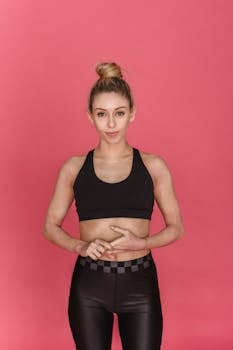 Young female athlete wearing black sports bra and leggings standing in studio against pink background and looking at camera