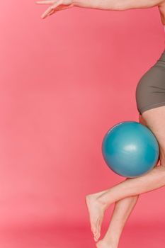 Side view of crop anonymous female athlete with outstretched arm lifting fitness ball against pink background