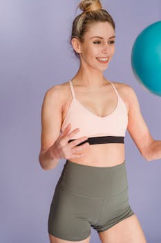 Smiling woman in activewear skillfully playing with a fitness ball in studio.