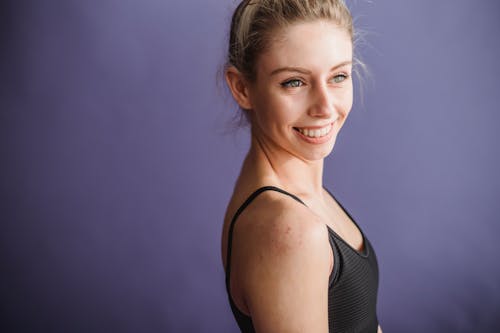 Free Happy crop slender female in black activewear smiling and looking away on purple background Stock Photo