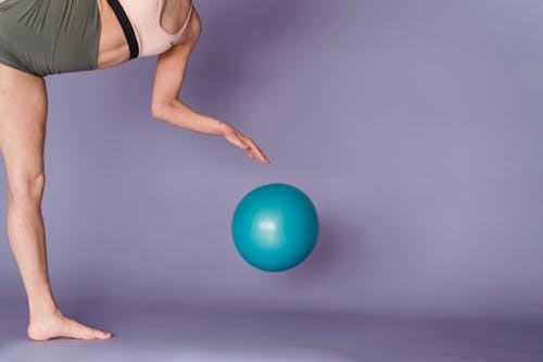 Free Side view of crop anonymous strong gymnast performing exercise with gym ball on purple background Stock Photo
