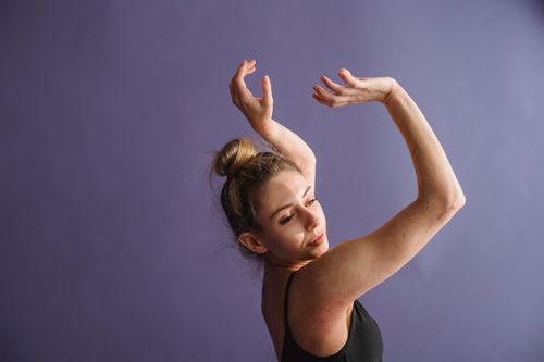 Free Side view of graceful slim dancer in black underwear dancing in studio against purple background and looking away Stock Photo