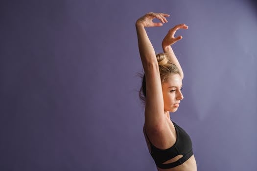 Side view of slim dancer in activewear standing with raised arms and dancing in studio against purple background