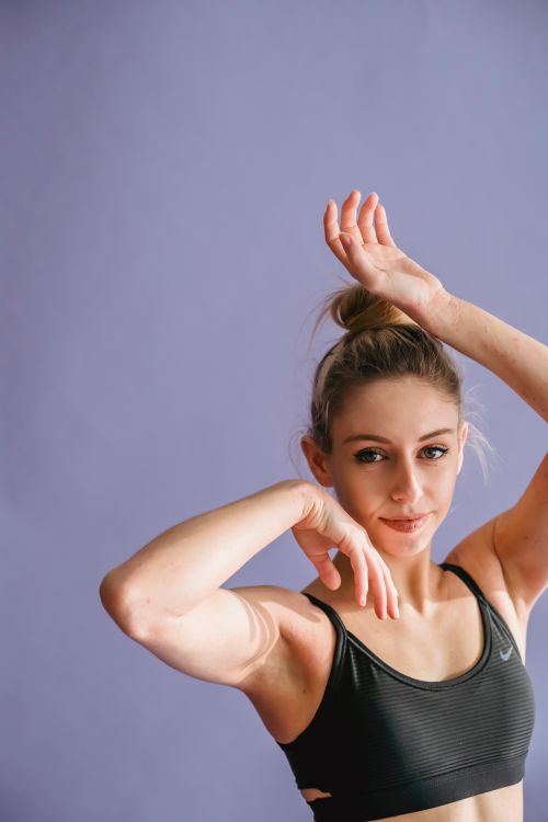Free Calm young female dancer in sportswear standing with raised arms and looking at camera against purple background in studio Stock Photo