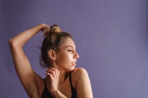 Free Tranquil young woman standing with raised arms and looking away against purple background in studio Stock Photo