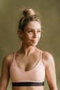 Young slim woman in sportswear with bare shoulders looking away against gray background in studio