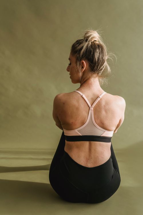 Free Back view of graceful young woman in activewear sitting on floor and looking away after yoga practice in studio Stock Photo
