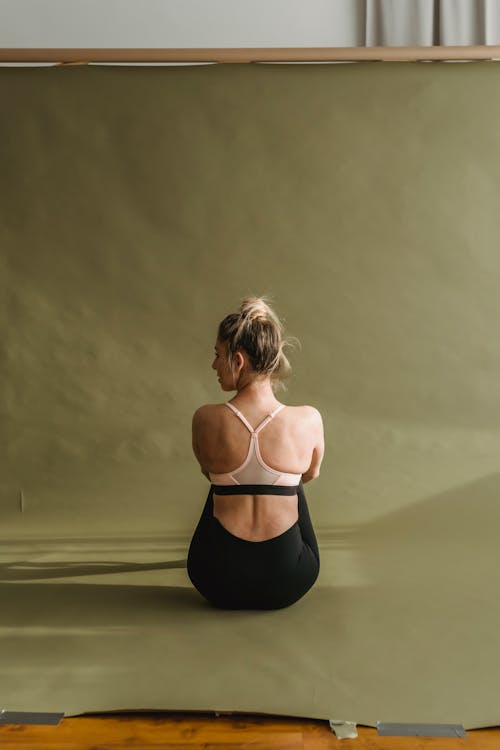Back view of young calm female athlete with blond in activewear sitting on floor after workout in studio