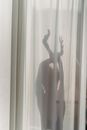 Shadow of anonymous female dancer performing sensual movements behind translucent white curtains in sunlight