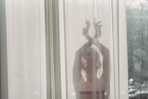 Calm woman standing behind tulle with hands above head