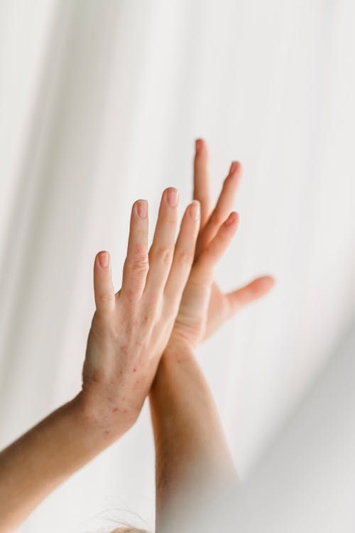 Hands of unrecognizable person with graceful gesture standing with raised arms near window with white curtain in light room at home