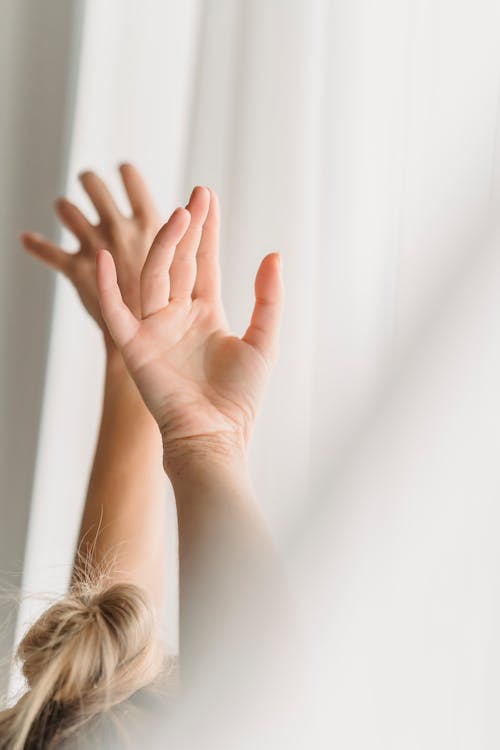 Crop woman with raised arms near curtain