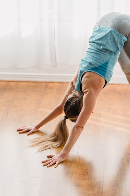 Free Side view of unrecognizable sportive fit female in activewear doing Downward facing dog while practicing yoga asana in light room Stock Photo