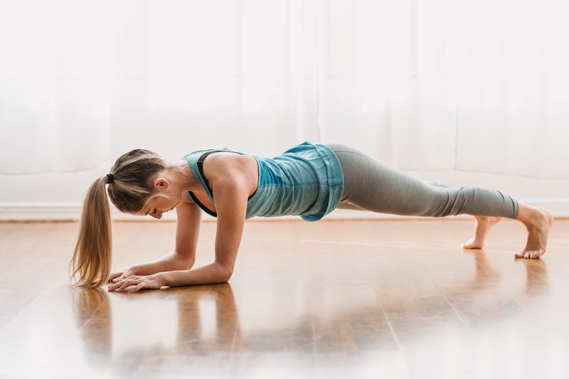 Woman doing a forearm plank on the floor at home — intense bodyweight workout with no equipment