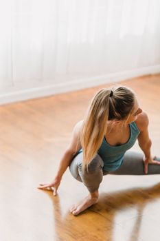 From above of slim female in activewear warming up and stretching on parquet in daytime