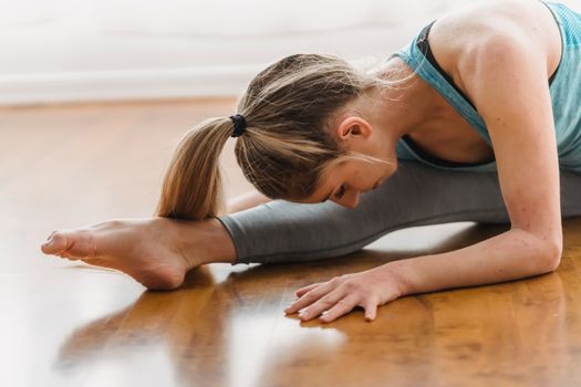 Side view of flexible barefoot female in activewear sitting in twine and bending over to leg