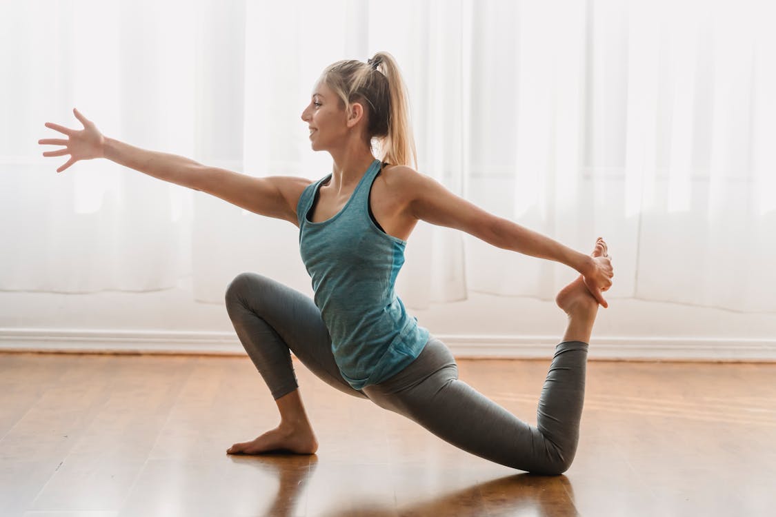 Side view of young slim female in sportswear smiling and looking forward while practicing yoga exercise