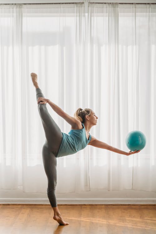 Side view of full body of fit female athlete balancing on tiptoe while doing exercise with gymnastic ball