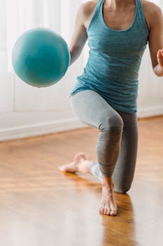 Faceless slim barefoot female in sportswear doing lunge exercise with fitness ball on floor during training in room at home