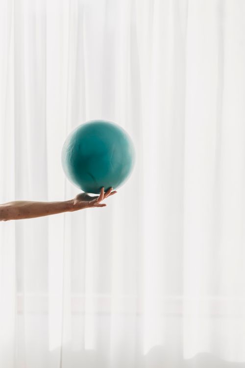 Free Crop faceless female athlete standing in front of big window with light curtain in daytime and holding ball on fingers Stock Photo