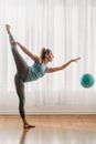 Side view of young flexible female in leggings raising leg behind back while performing exercise with gymnastic ball